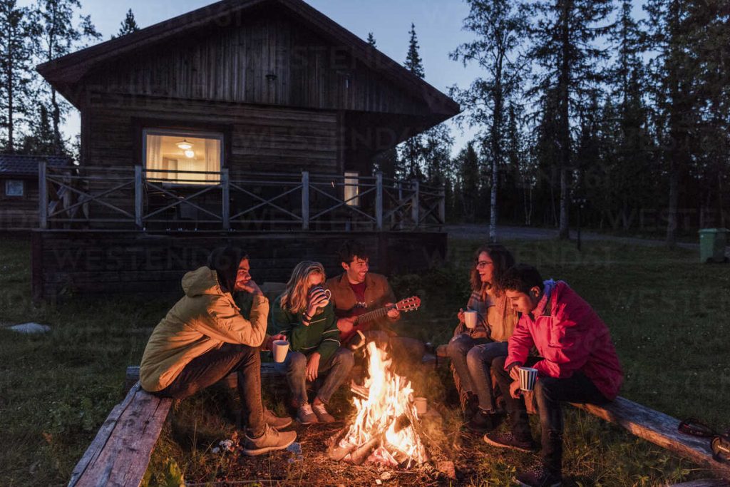 Group of friends sitting at a campfire, talking and playing guitar